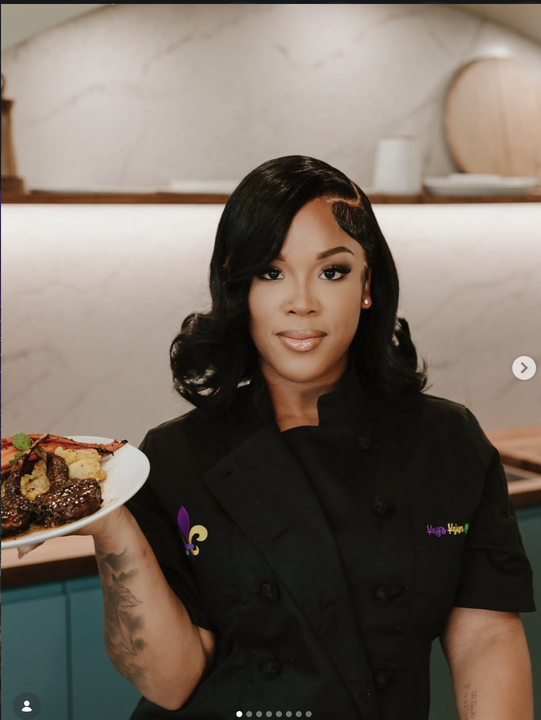 Chef Kayla Powell in a black chef coat holding a plated entrée